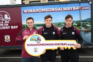 Galway footballers Cillian McDaid, Cillian Ó Curraoin and Matthew Thompson holding a giant WinAHomeOnGalwayBay.com key in front of the campaign van