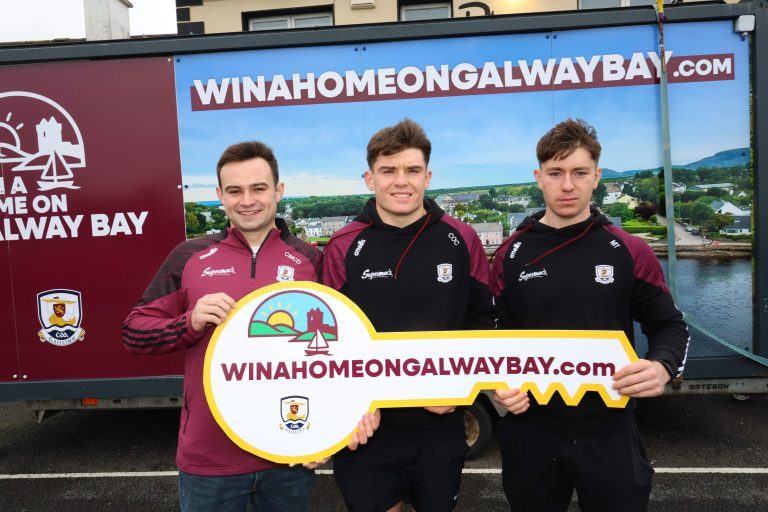 Galway footballers Cillian McDaid, Cillian Ó Curraoin and Matthew Thompson holding a giant WinAHomeOnGalwayBay.com key in front of the campaign van